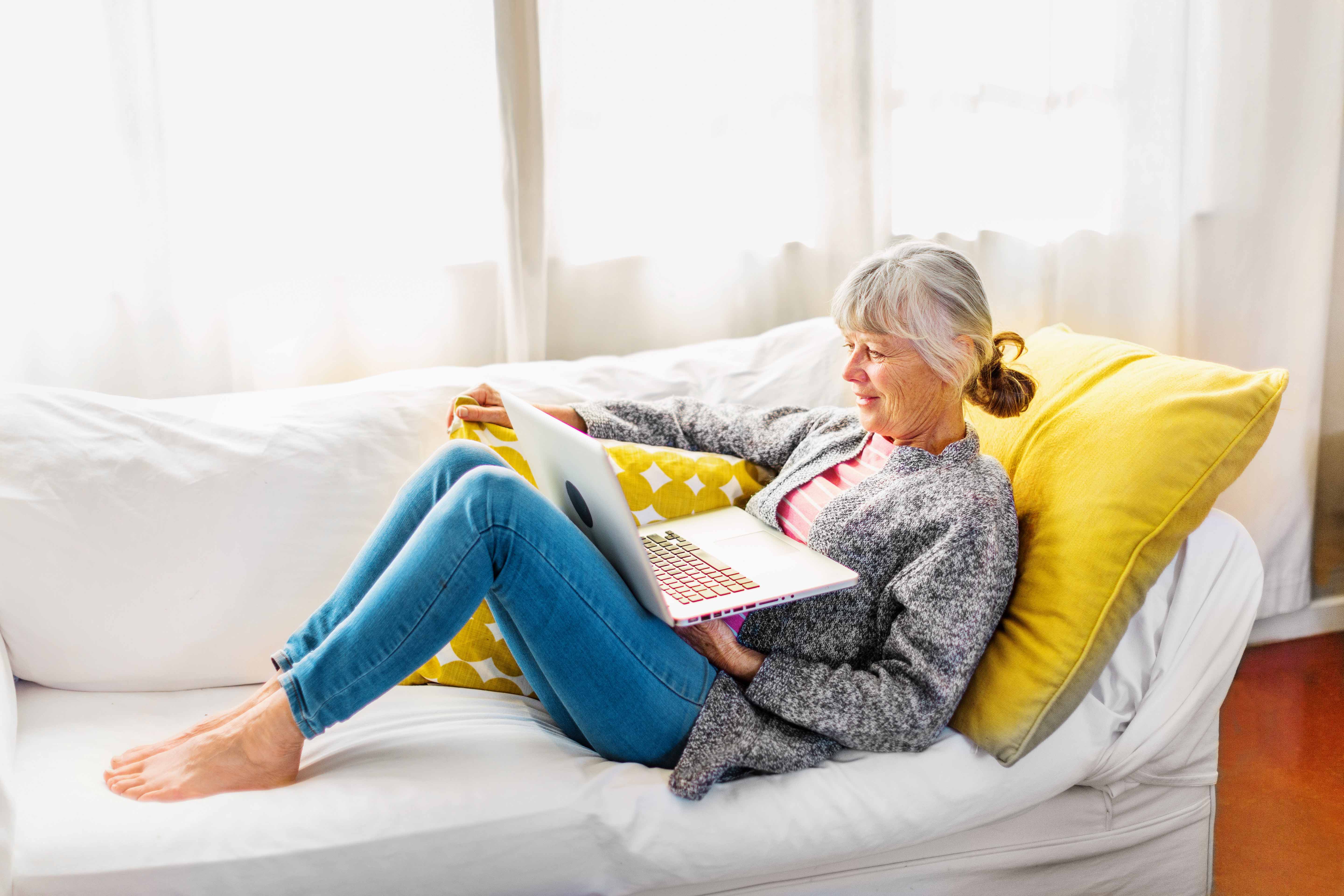 Woman using laptop on couch in sunny room