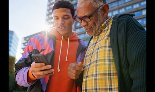 Casual portrait of a young man showing an older man something on his phone, shot on a sunny day in the city
